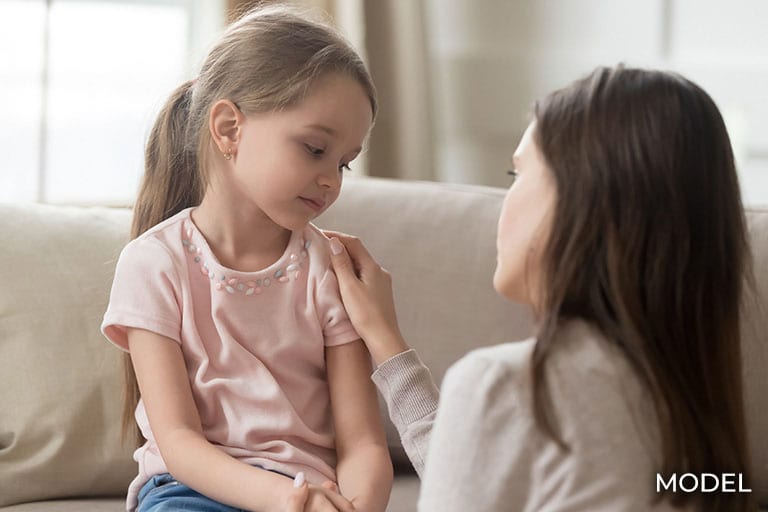 Loving mom talking to upset little girl at home on couch